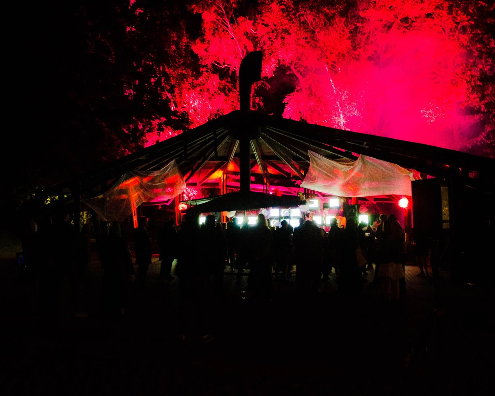 Drewniana scena nocą w czerwonym świetle laserów, sylwetki publiczności
